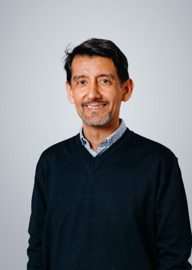 A man with dark coloured hair in a dark blue jumper, smiling